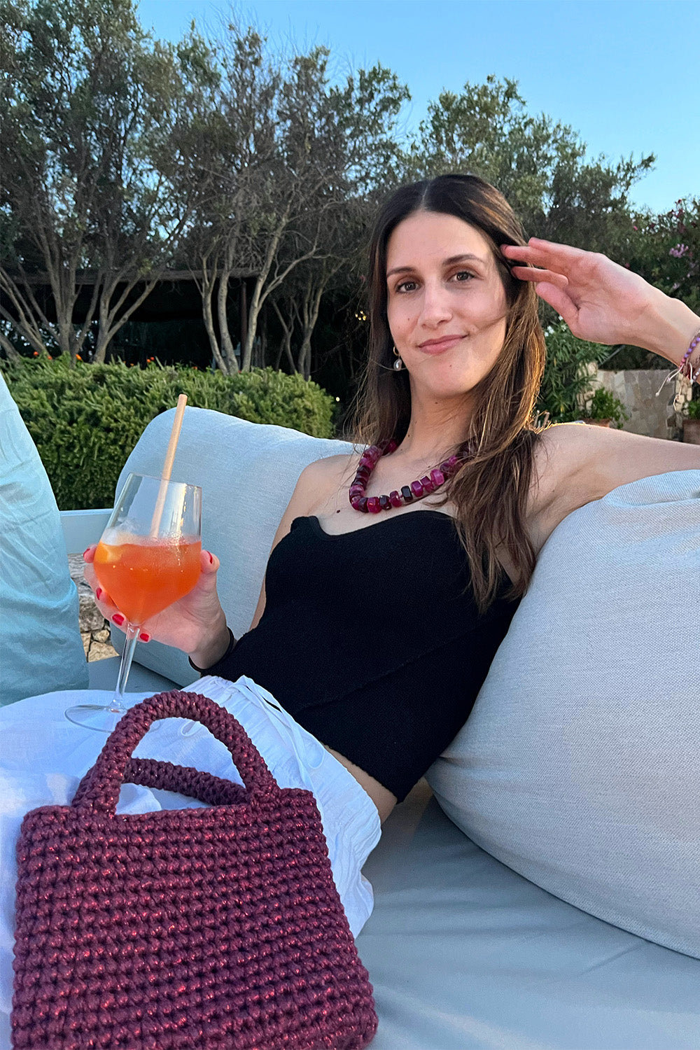 Mujer usando una cartera tejida color guinda metalizado.