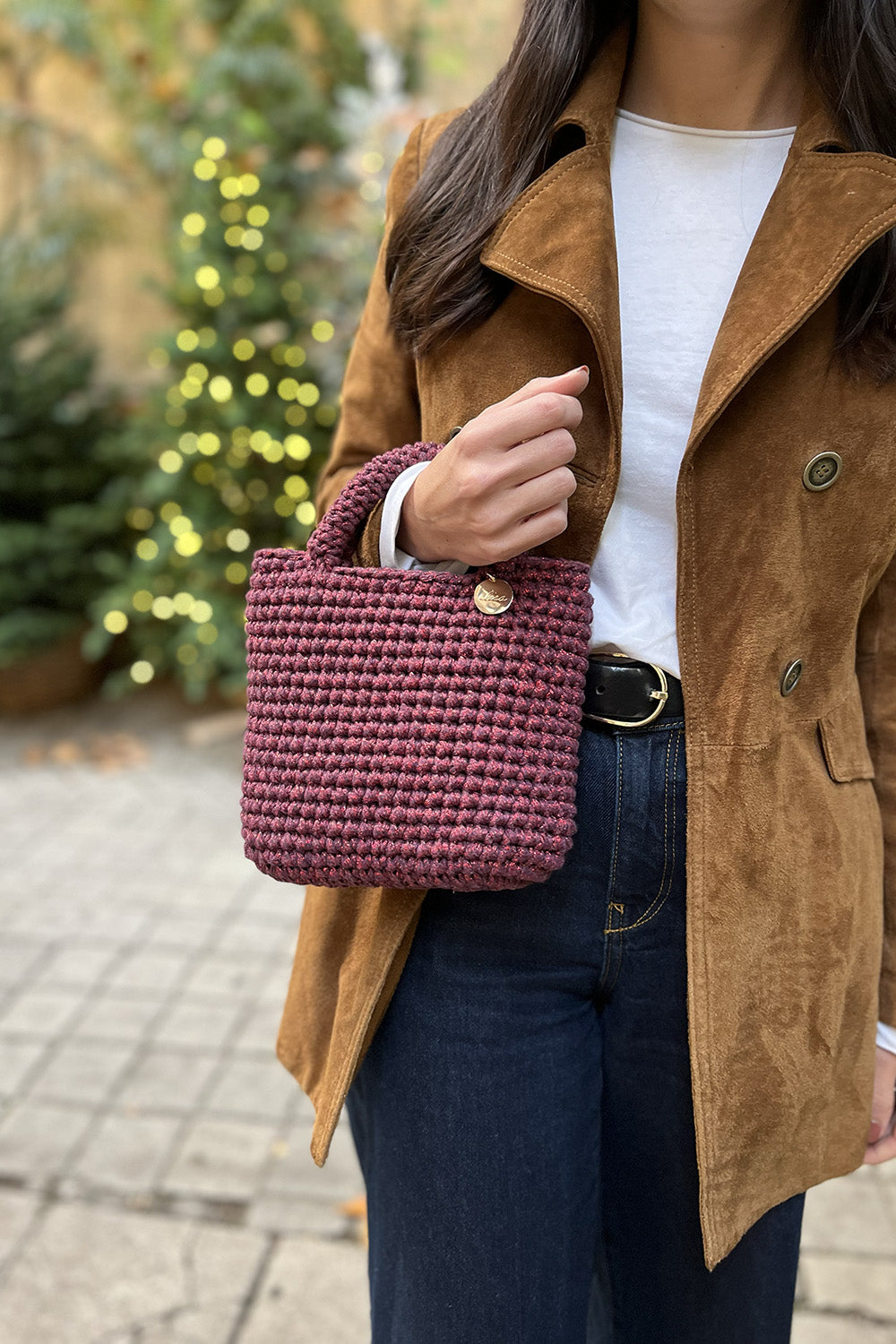 Mujer usando una cartera tejida color guinda metalizado.