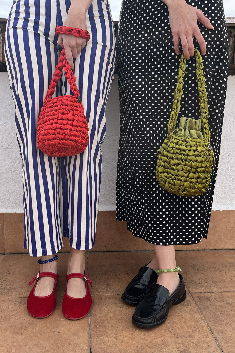 Dos mujeres sujetando carteras tejidas. Una de las carteras es color rojo y la otra es color pistachio.